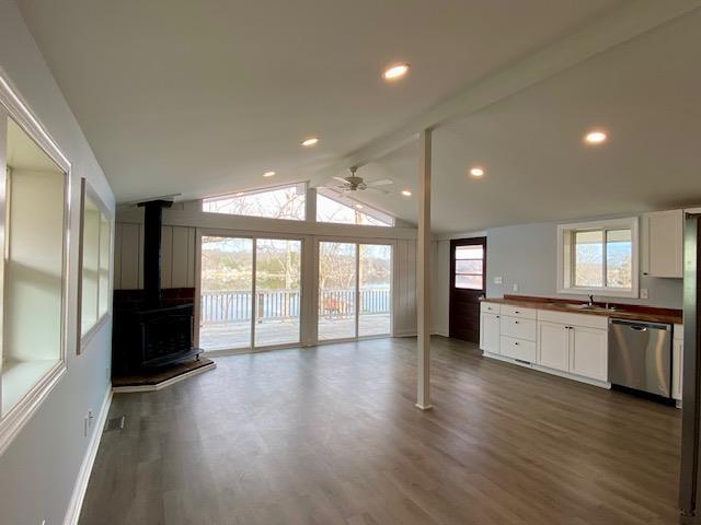 unfurnished living room featuring a wood stove, vaulted ceiling with beams, dark hardwood / wood-style floors, and ceiling fan