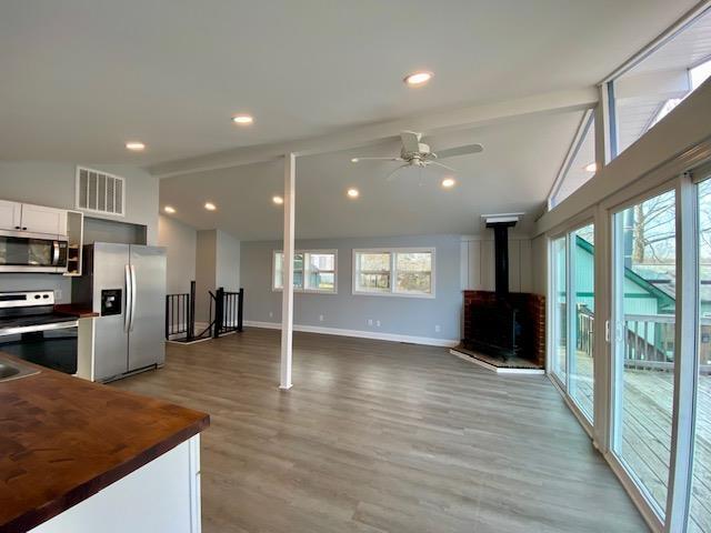 kitchen with appliances with stainless steel finishes, vaulted ceiling with beams, butcher block counters, white cabinets, and a wood stove