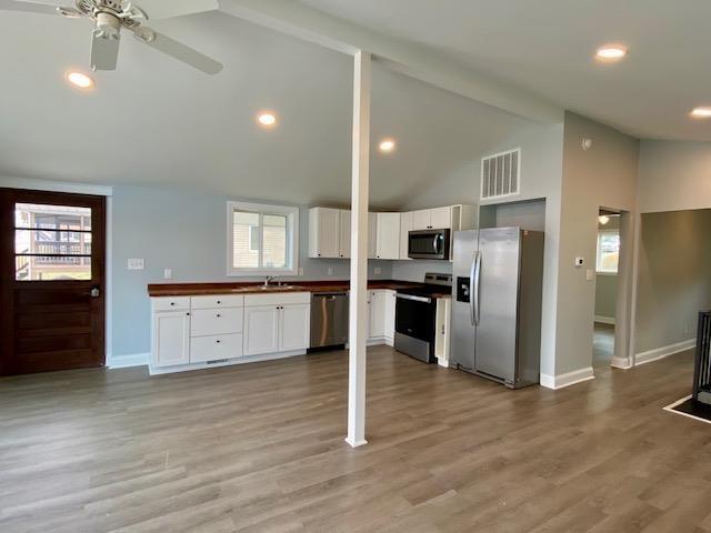 kitchen with white cabinetry, appliances with stainless steel finishes, light wood-type flooring, and lofted ceiling