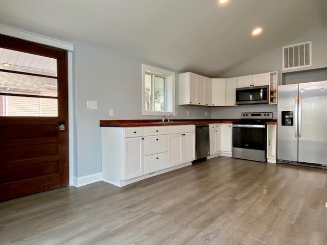 kitchen with vaulted ceiling, light hardwood / wood-style flooring, sink, white cabinetry, and stainless steel appliances