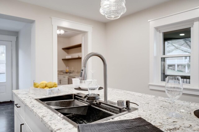 interior details featuring white cabinetry, light stone countertops, sink, and a notable chandelier