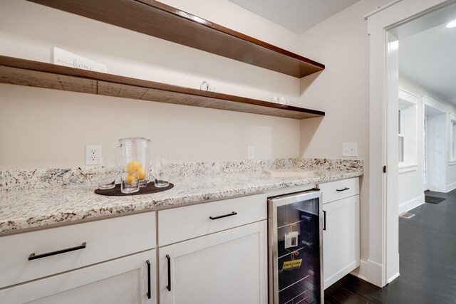 bar with dark hardwood / wood-style floors, light stone countertops, beverage cooler, and white cabinets