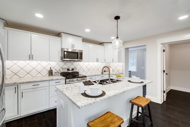 kitchen featuring white cabinetry, appliances with stainless steel finishes, a kitchen island with sink, and pendant lighting