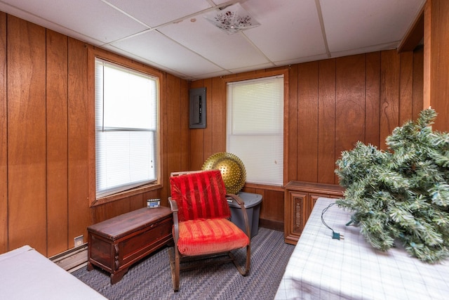 sitting room featuring a baseboard heating unit, wooden walls, and a drop ceiling