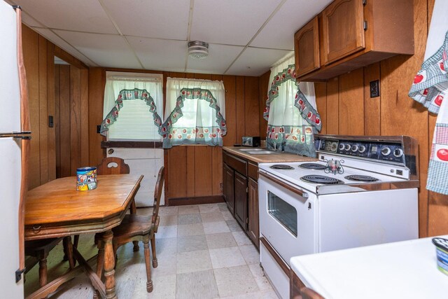 kitchen with sink, a paneled ceiling, wood walls, and white range with electric cooktop