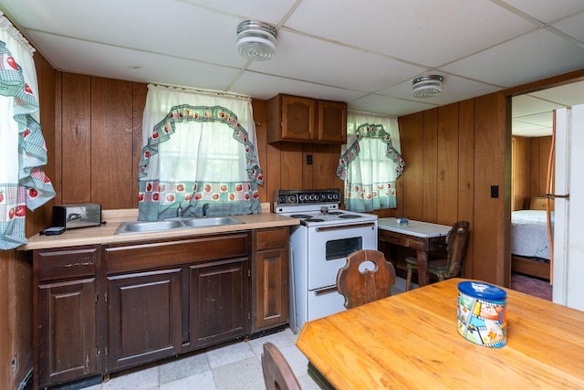 kitchen with a drop ceiling, sink, white appliances, and wood walls