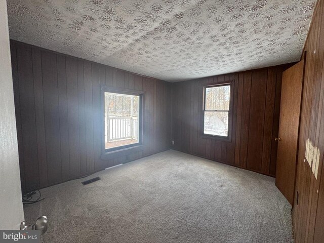 unfurnished room with light carpet, a textured ceiling, and wood walls