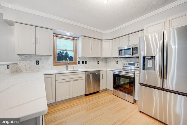 kitchen featuring sink, light hardwood / wood-style flooring, appliances with stainless steel finishes, ornamental molding, and white cabinets