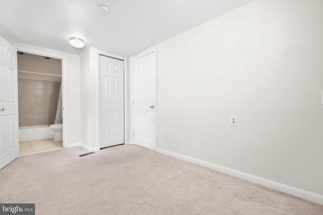 unfurnished bedroom with light carpet, ensuite bath, and a closet