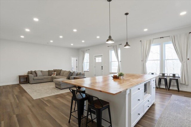 kitchen with dark wood-type flooring, wood counters, white cabinetry, a center island, and pendant lighting