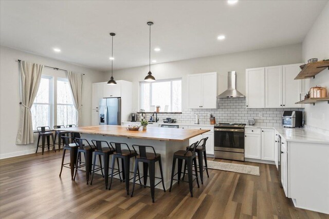 kitchen featuring wall chimney exhaust hood, decorative light fixtures, appliances with stainless steel finishes, a kitchen island, and white cabinets