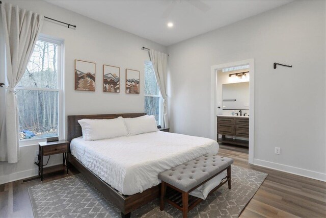 bedroom with ensuite bathroom, dark hardwood / wood-style flooring, sink, and multiple windows