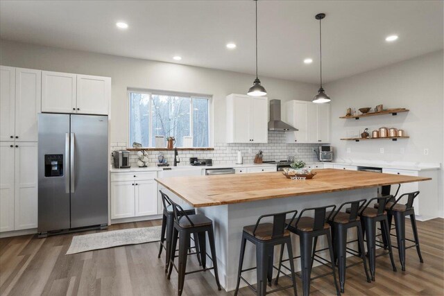 kitchen featuring white cabinetry, a kitchen island, stainless steel fridge, and wall chimney exhaust hood