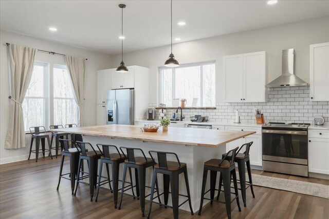 kitchen with stainless steel appliances, white cabinetry, a kitchen island, and wall chimney exhaust hood