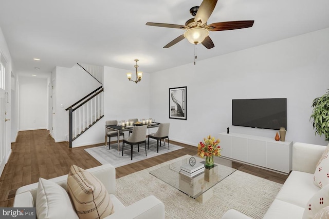 living room featuring stairway, wood finished floors, baseboards, recessed lighting, and ceiling fan with notable chandelier