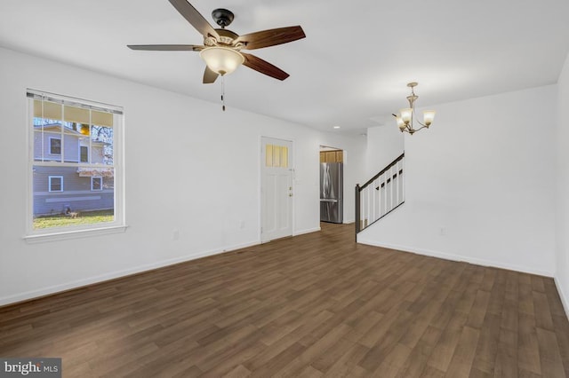 unfurnished living room featuring stairs, ceiling fan with notable chandelier, dark wood-style floors, and baseboards