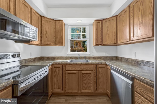 kitchen featuring a sink, dark countertops, appliances with stainless steel finishes, and brown cabinetry