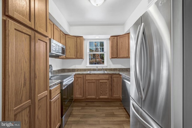 kitchen featuring dark countertops, brown cabinetry, appliances with stainless steel finishes, and a sink