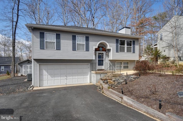 split foyer home featuring aphalt driveway, central AC unit, an attached garage, and a chimney