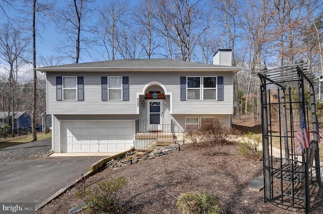 bi-level home with a garage, driveway, and a chimney