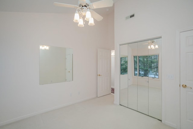 unfurnished bedroom with a towering ceiling, light carpet, ceiling fan, and a closet