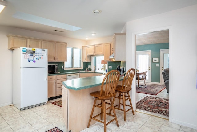 kitchen featuring a kitchen bar, white appliances, a skylight, and light brown cabinets