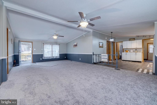 unfurnished living room featuring rail lighting, ceiling fan, carpet, lofted ceiling with beams, and a textured ceiling