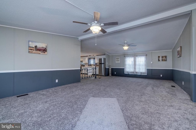 unfurnished living room with ceiling fan, carpet flooring, a textured ceiling, and vaulted ceiling with beams