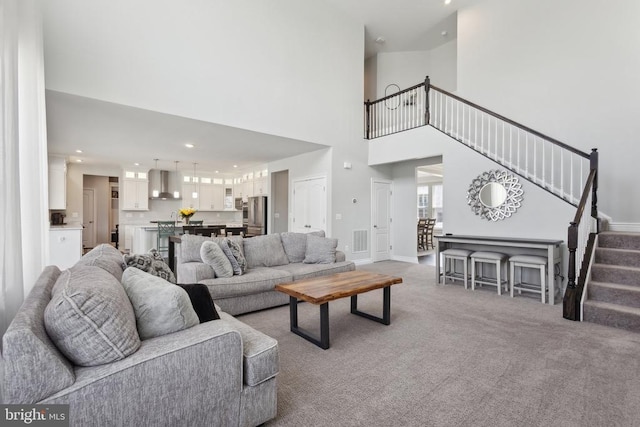 carpeted living room with stairway, a high ceiling, visible vents, and recessed lighting