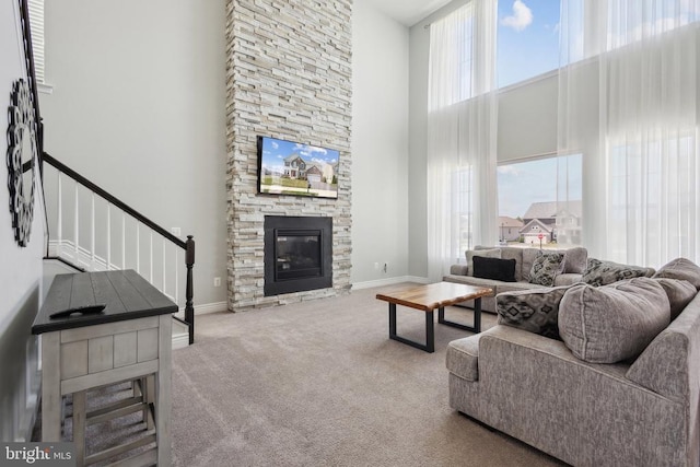 carpeted living area featuring stairway, a high ceiling, baseboards, and a stone fireplace