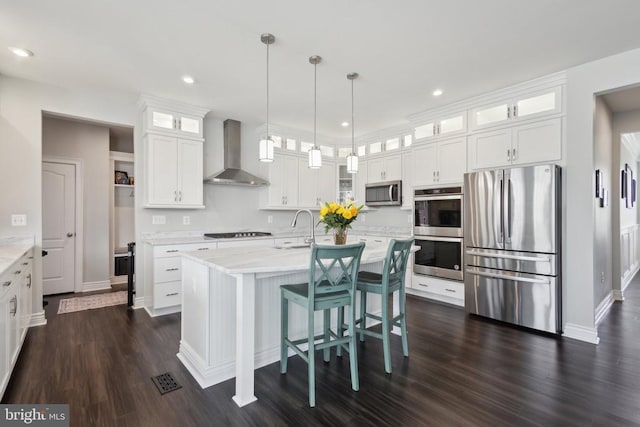 kitchen with a sink, stainless steel appliances, white cabinetry, dark wood-type flooring, and wall chimney range hood