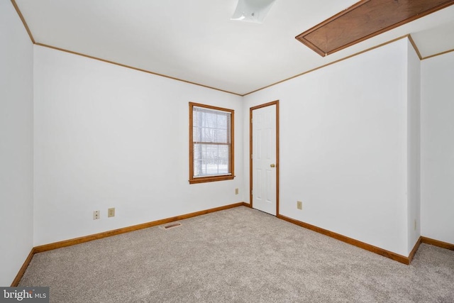 carpeted empty room featuring visible vents, attic access, crown molding, and baseboards