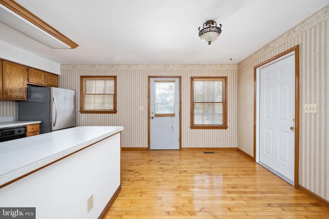 kitchen with light countertops, light wood finished floors, brown cabinets, and freestanding refrigerator