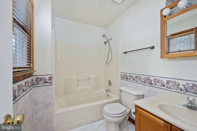 bathroom with toilet, marble finish floor, washtub / shower combination, wainscoting, and vanity