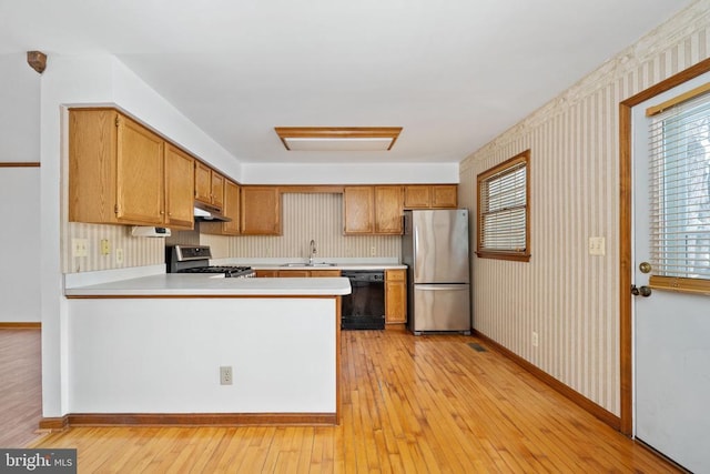 kitchen with a sink, light countertops, under cabinet range hood, appliances with stainless steel finishes, and light wood-type flooring