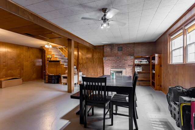 dining space featuring ceiling fan, a brick fireplace, and wood walls