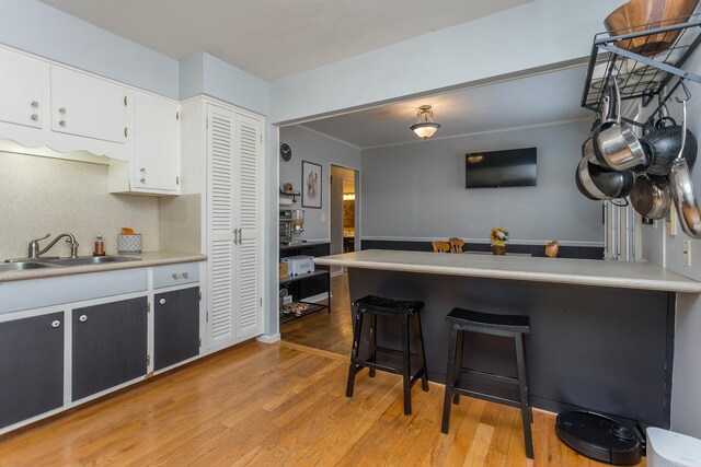 kitchen featuring sink, white cabinetry, light wood-type flooring, a kitchen breakfast bar, and backsplash