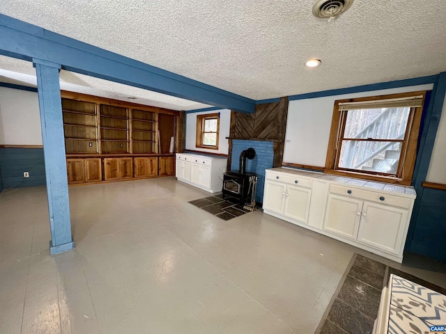 interior space featuring a textured ceiling, a wood stove, visible vents, and white cabinets