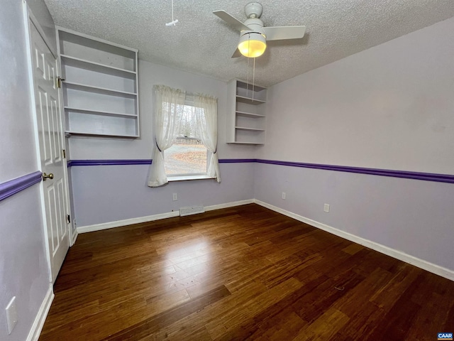 empty room with visible vents, dark wood-type flooring, a ceiling fan, a textured ceiling, and baseboards