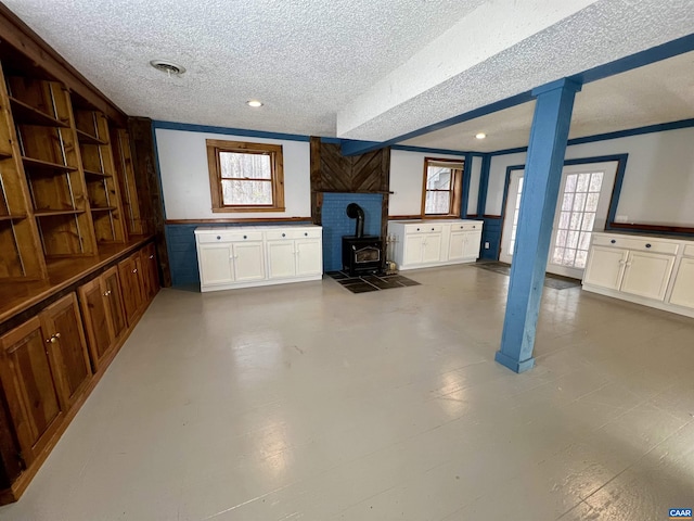 unfurnished living room with a textured ceiling, visible vents, ornamental molding, wainscoting, and a wood stove