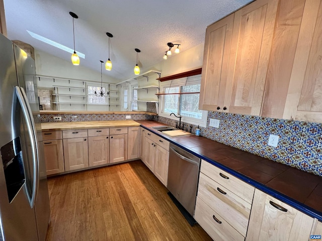 kitchen with appliances with stainless steel finishes, hanging light fixtures, a sink, and light brown cabinetry