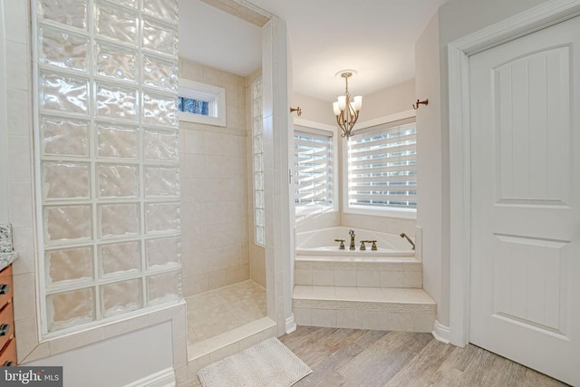 bathroom with wood finished floors, a garden tub, walk in shower, vanity, and a chandelier