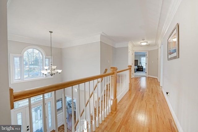 hall featuring crown molding, an inviting chandelier, light wood-style floors, an upstairs landing, and baseboards