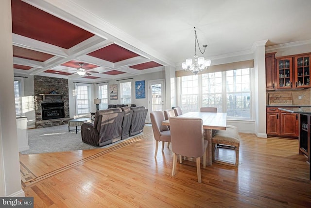 dining area with a fireplace, coffered ceiling, light wood-style floors, beamed ceiling, and crown molding