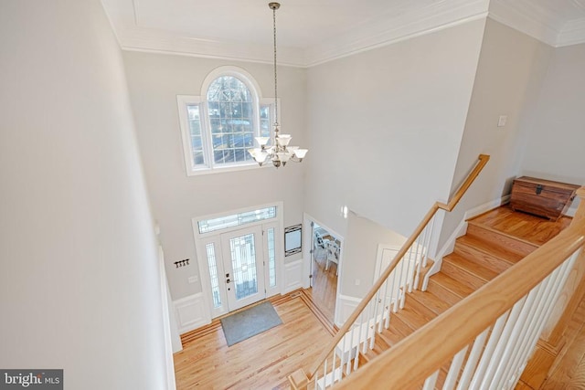 entryway featuring a towering ceiling, wood finished floors, an inviting chandelier, stairs, and crown molding