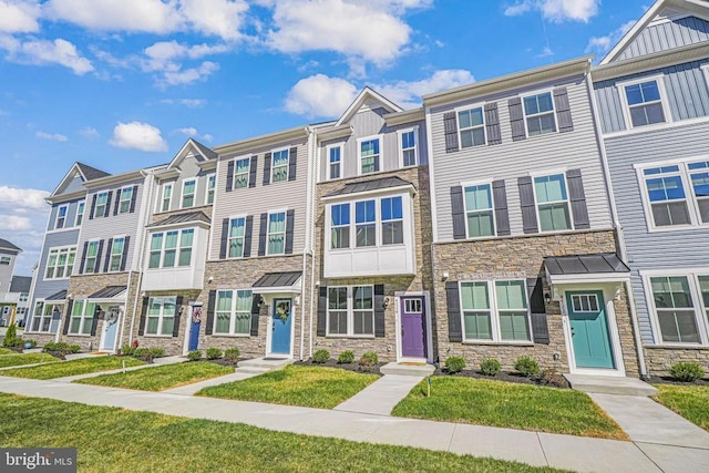 townhome / multi-family property featuring a standing seam roof, stone siding, board and batten siding, a front lawn, and a residential view