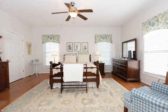 bedroom with baseboards, ceiling fan, multiple windows, and wood finished floors