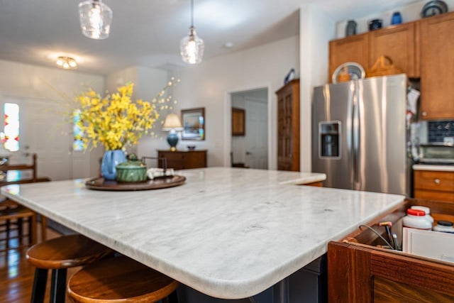 kitchen featuring brown cabinets, hanging light fixtures, a kitchen bar, and stainless steel refrigerator with ice dispenser
