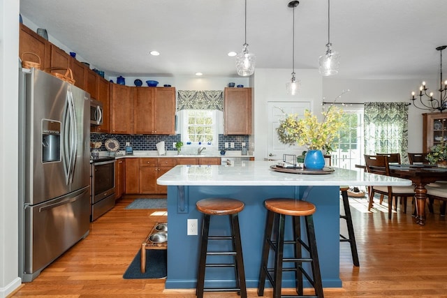 kitchen with a kitchen bar, light wood-type flooring, light countertops, tasteful backsplash, and appliances with stainless steel finishes