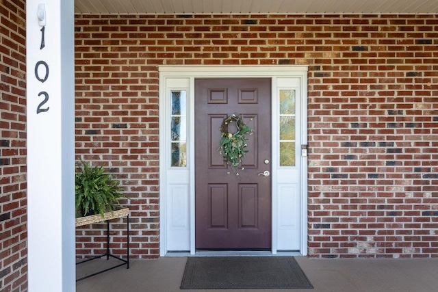 view of exterior entry featuring covered porch and brick siding